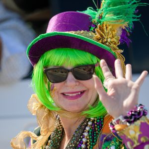 mardi gras parade sites and sounds including purple, gold, and green hats, beads, and clothes worn by various parade goers.