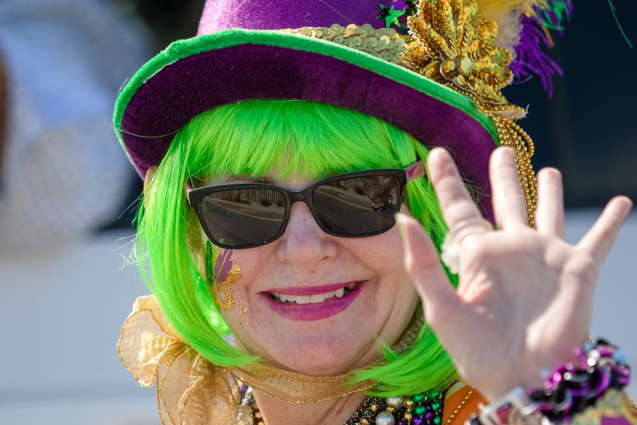 mardi gras parade sites and sounds including purple, gold, and green hats, beads, and clothes worn by various parade goers.