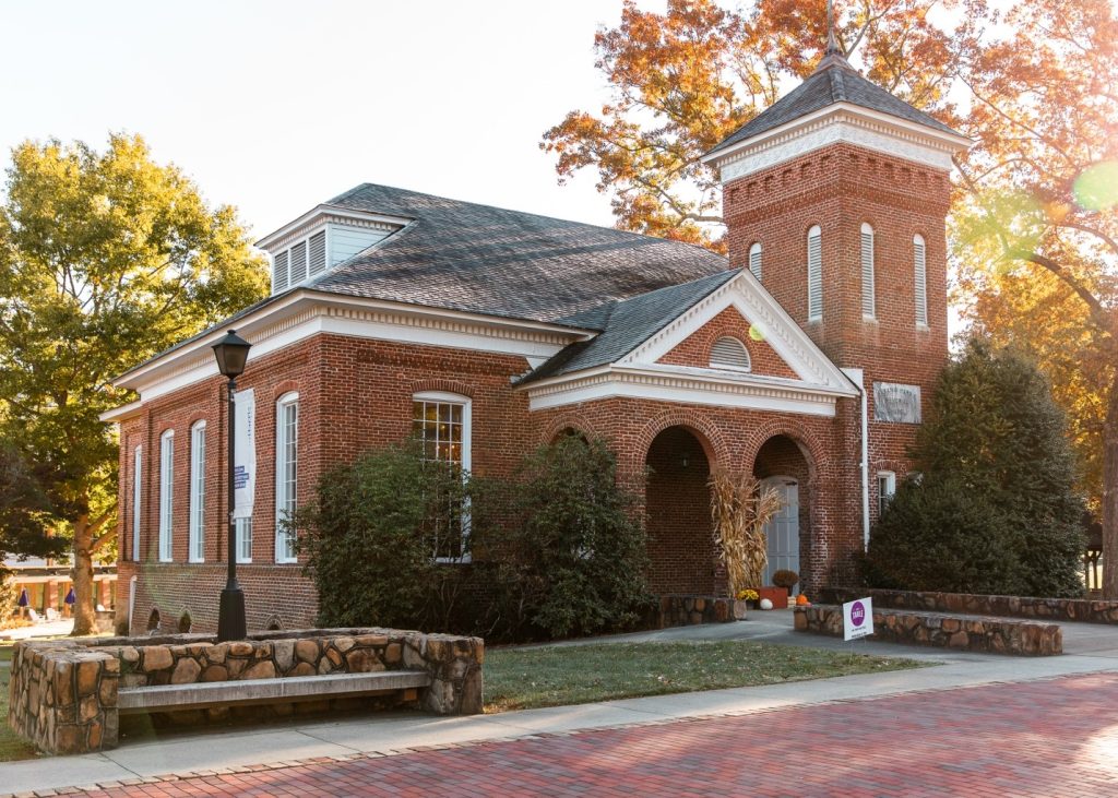 Historic brick building with white trim and a clock tower, surrounded by autumn foliage, at Young Harris College during the fall season, reflecting a serene academic setting