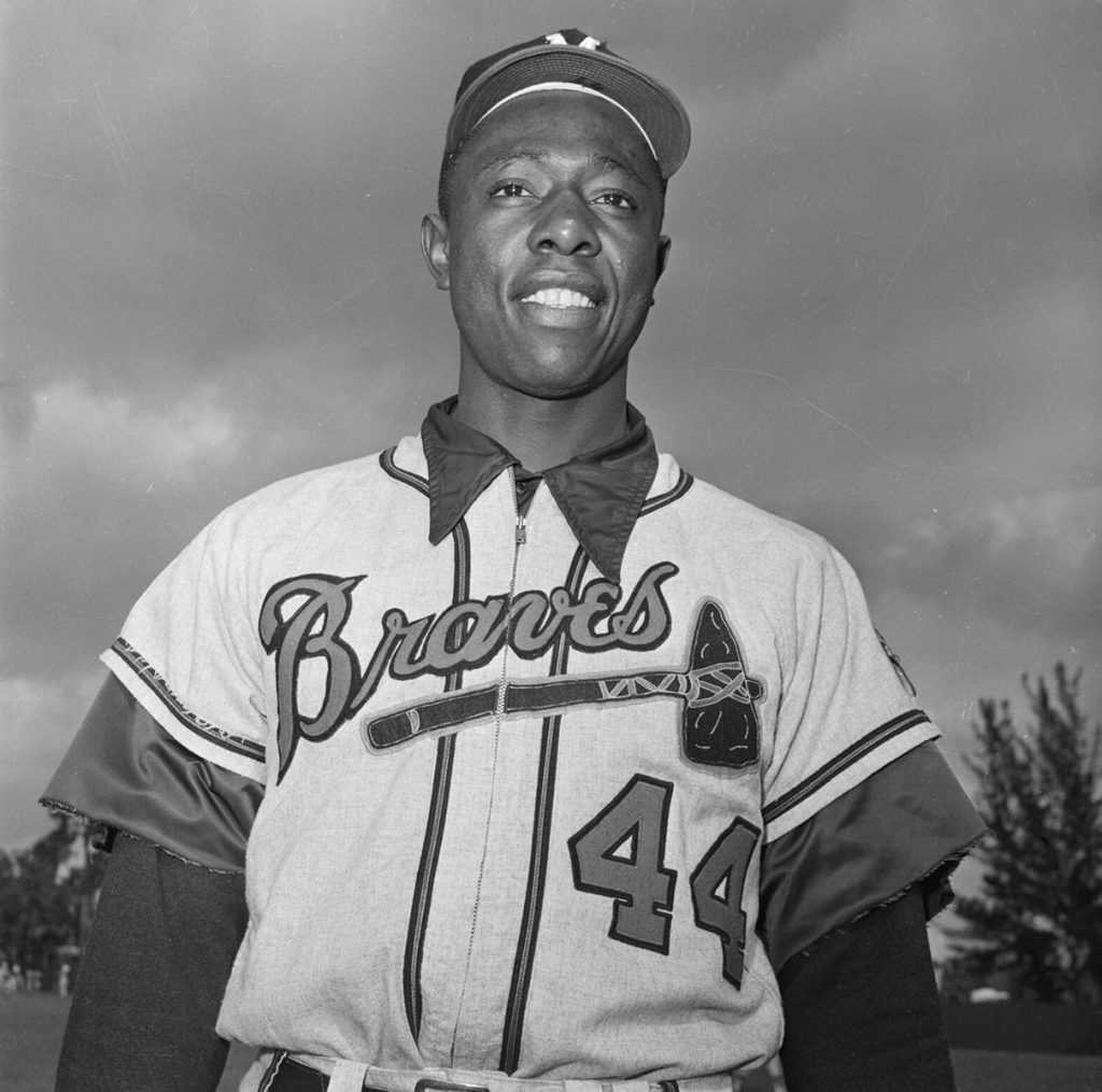 Hank Aaron, wearing the No. 44 Atlanta Braves jersey, standing on the field during a sunny day.